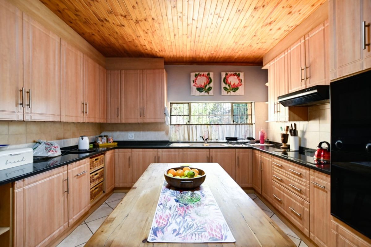 A functional kitchen featuring light wood cabinetry, dark granite countertops, a double sink, and a warm wooden tongue and groove ceiling.