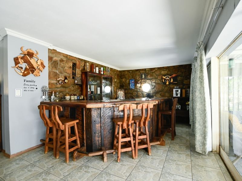 A rustic indoor bar area featuring a substantial built-in wooden counter, stone-clad feature wall, and tiled flooring with access to the outdoors via sliding doors.