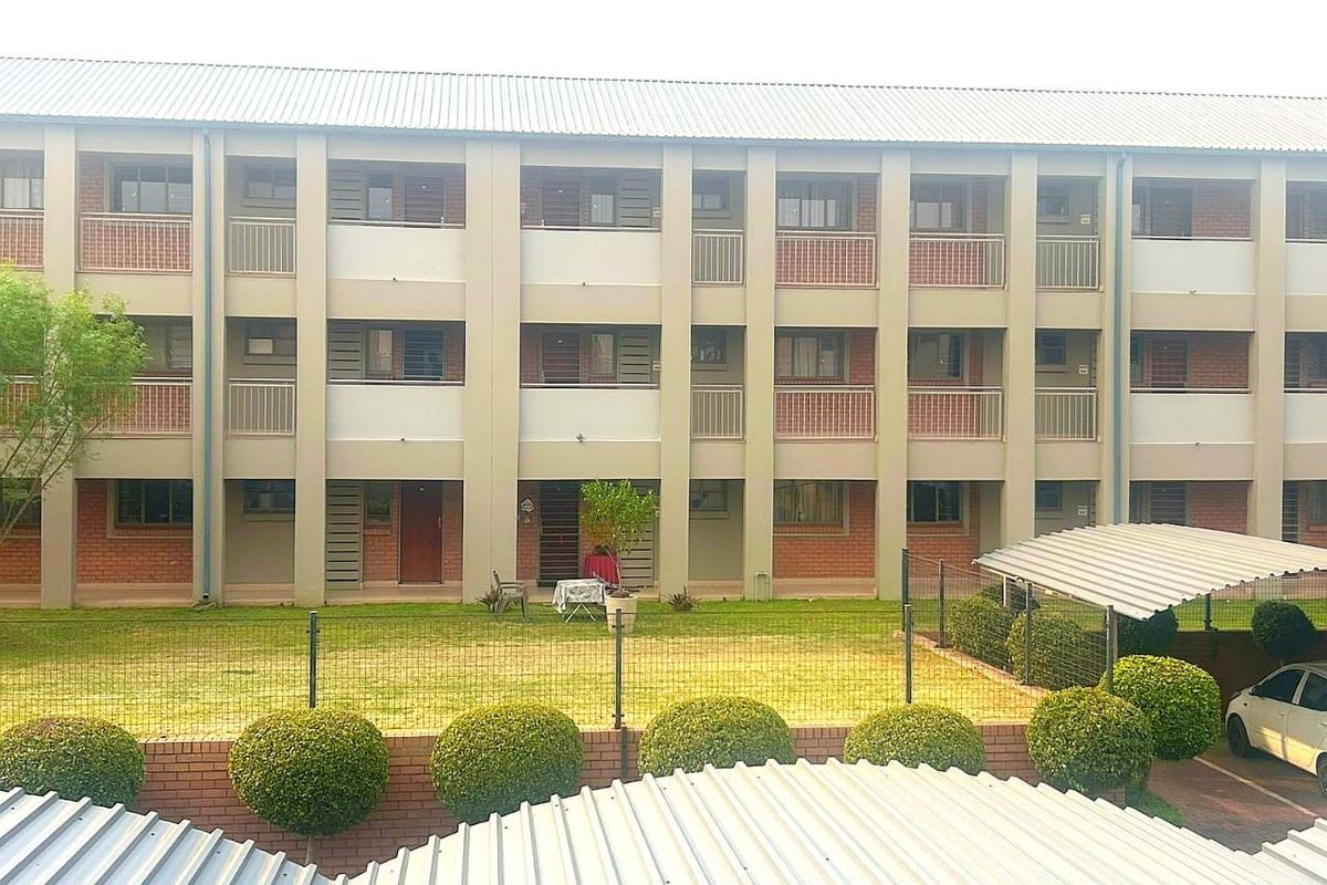 A view of the apartment building exterior featuring brick and plaster facade, private balconies, and a covered carport area.