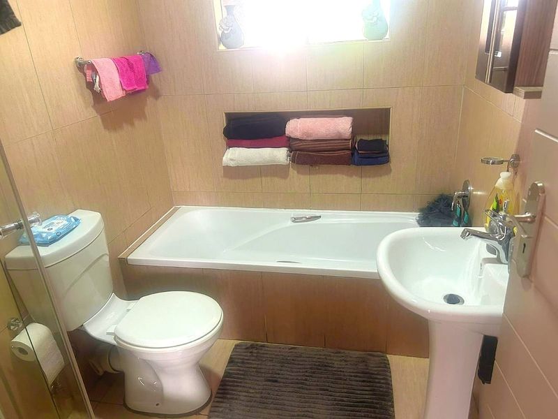A functional bathroom featuring a bathtub, pedestal sink, toilet, and tiled finishes with a convenient recessed wall niche for storage.