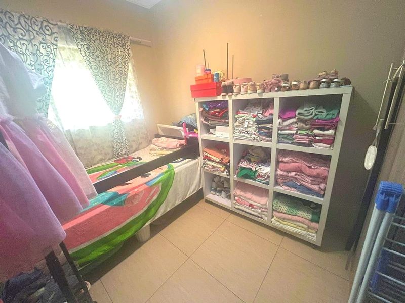 A bedroom featuring tiled flooring and a window, currently utilized as a child's room with storage shelving.