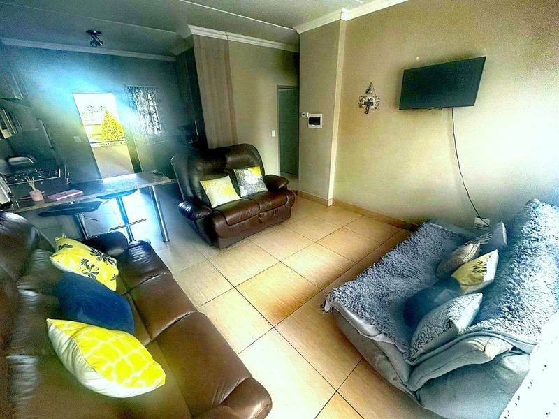 Open-plan living area featuring tiled flooring, coved cornicing, and an integrated kitchen space with a breakfast bar.