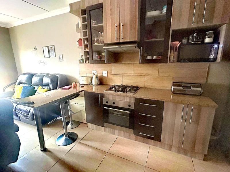 Open-plan kitchen featuring wood-finish cabinetry, granite countertops, gas hob, and integrated oven, seamlessly flowing into the adjacent living area with tiled flooring.