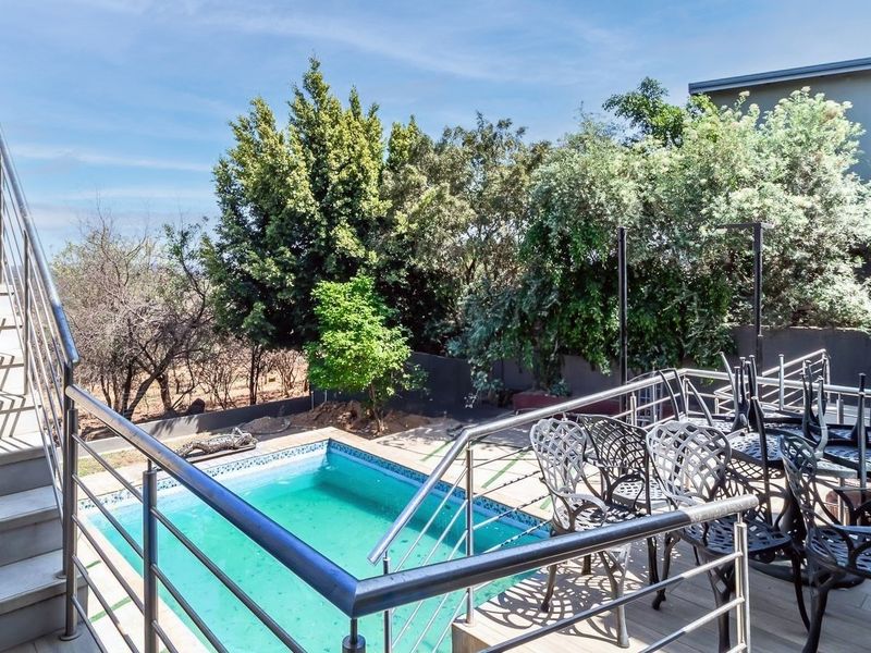 Outdoor entertainment area featuring a swimming pool, stainless steel balustrades, and a metal staircase leading to an elevated patio deck.