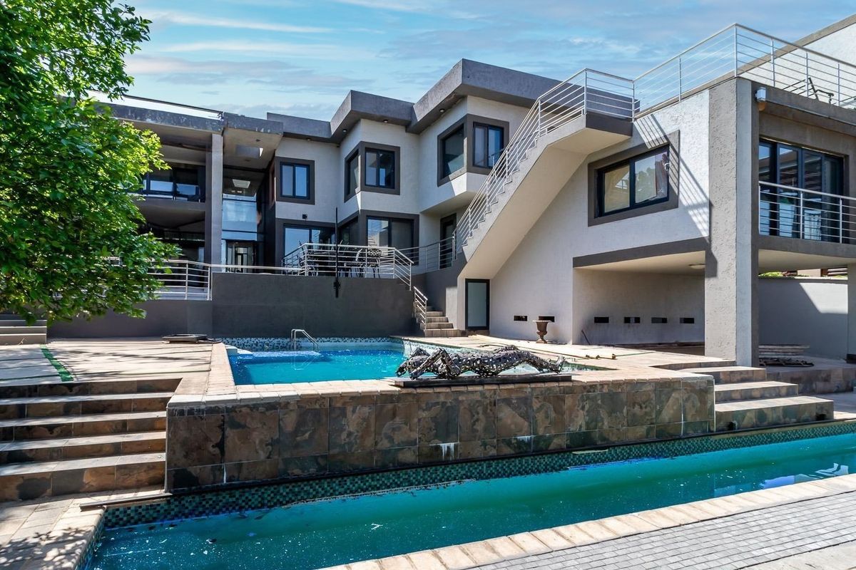 Rear exterior view of a modern multi-level home featuring a multi-tiered swimming pool, stone-clad pool surround, and an external staircase with metal railings.