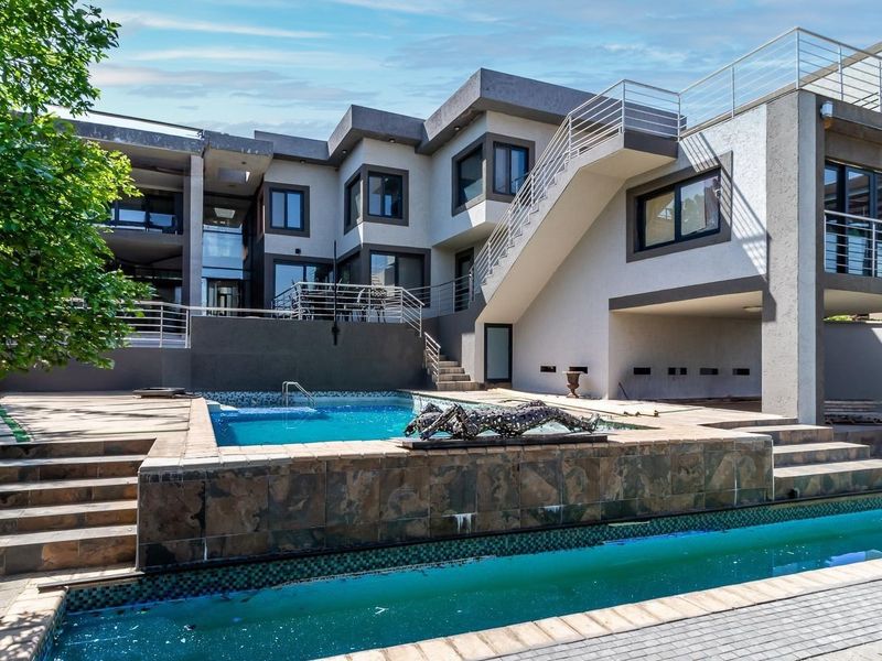 Rear exterior view of a modern multi-level home featuring a multi-tiered swimming pool, stone-clad pool surround, and an external staircase with metal railings.