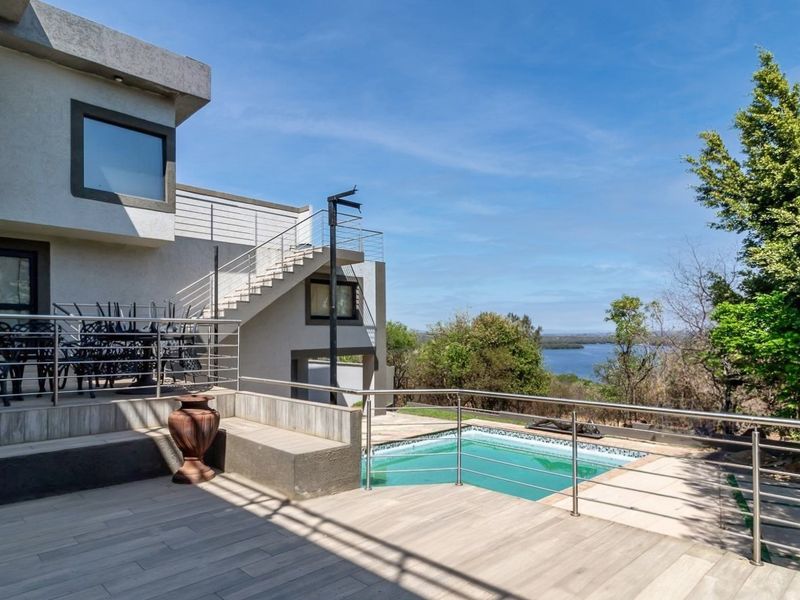 A modern outdoor entertainment area featuring a swimming pool, tiled patio, and stainless steel balustrades with scenic views.