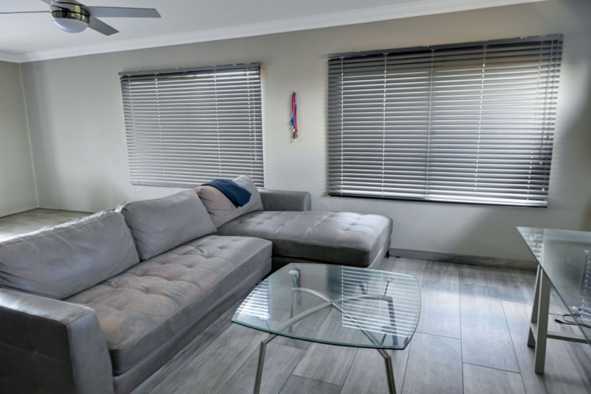 A well-lit living room featuring modern grey tiled flooring, neutral wall tones, and fitted venetian blinds.