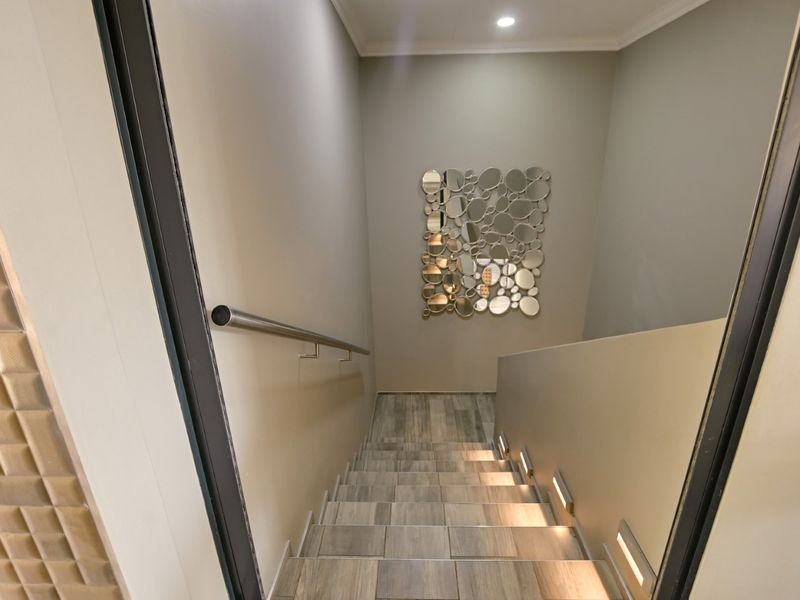 A modern staircase featuring tiled steps, integrated recessed lighting, and a sleek stainless steel handrail, providing a clean and contemporary transition between levels.