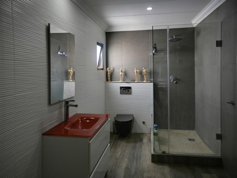 Modern bathroom featuring a walk-in glass shower, wall-mounted toilet, vanity unit with basin, and contemporary textured wall tiling.
