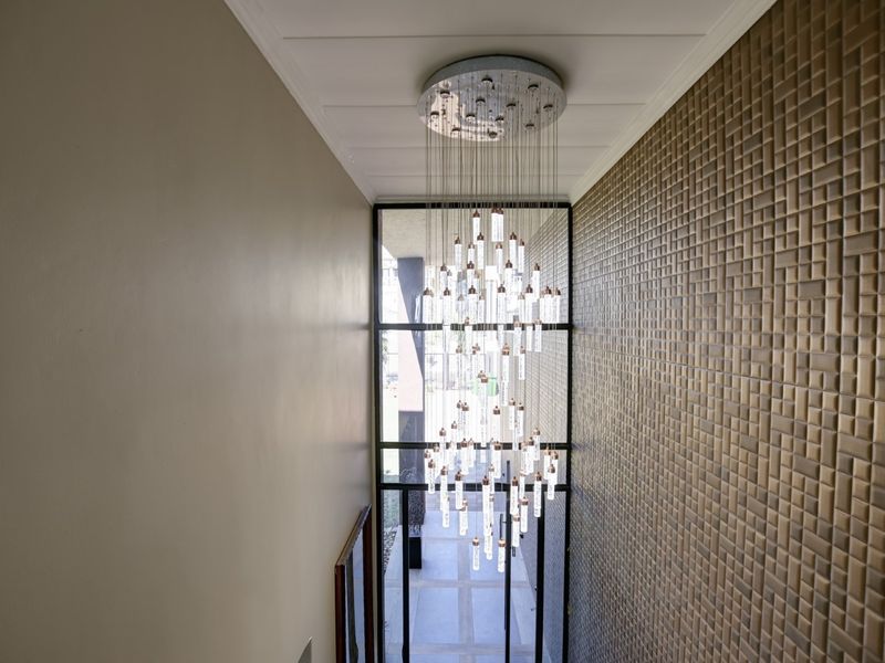 Elegant double-volume entrance hall featuring a striking modern chandelier, textured feature wall, and expansive glass window overlooking the exterior.