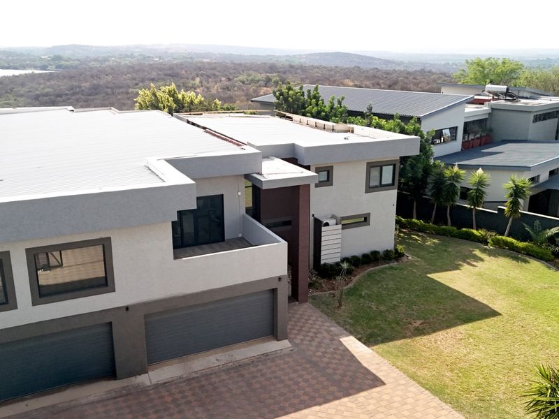 Aerial view of a modern multi-level residence featuring a double garage, paved driveway, and landscaped garden with scenic landscape views.