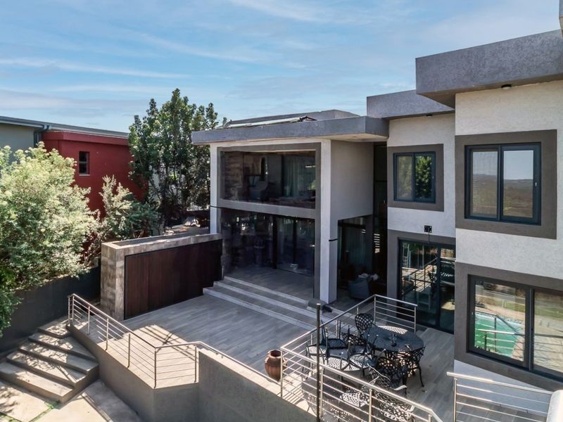 Rear view of a modern multi-level home featuring a spacious tiled patio, stainless steel balustrades, and large glass sliding doors.