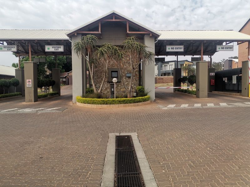The secure entrance gatehouse of the apartment complex, featuring paved driveway access, boom gates, and stone-clad architectural detailing.