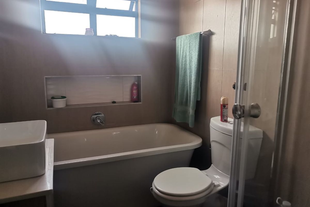 A functional bathroom featuring a bathtub, separate shower enclosure, wall-mounted basin, and a convenient recessed wall niche for storage.