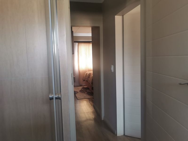 A view through a hallway leading towards a bedroom, featuring laminate flooring and neutral interior doors.
