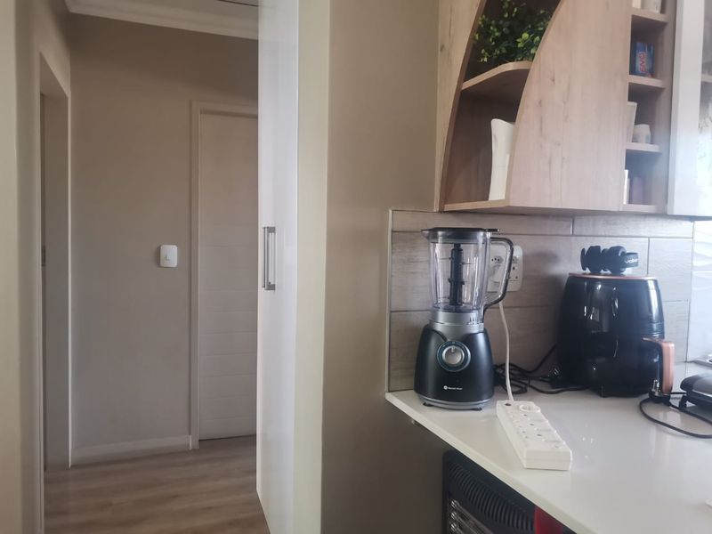 A functional kitchen area featuring built-in cabinetry, a tiled backsplash, and stone countertops, leading into a hallway with internal doors.