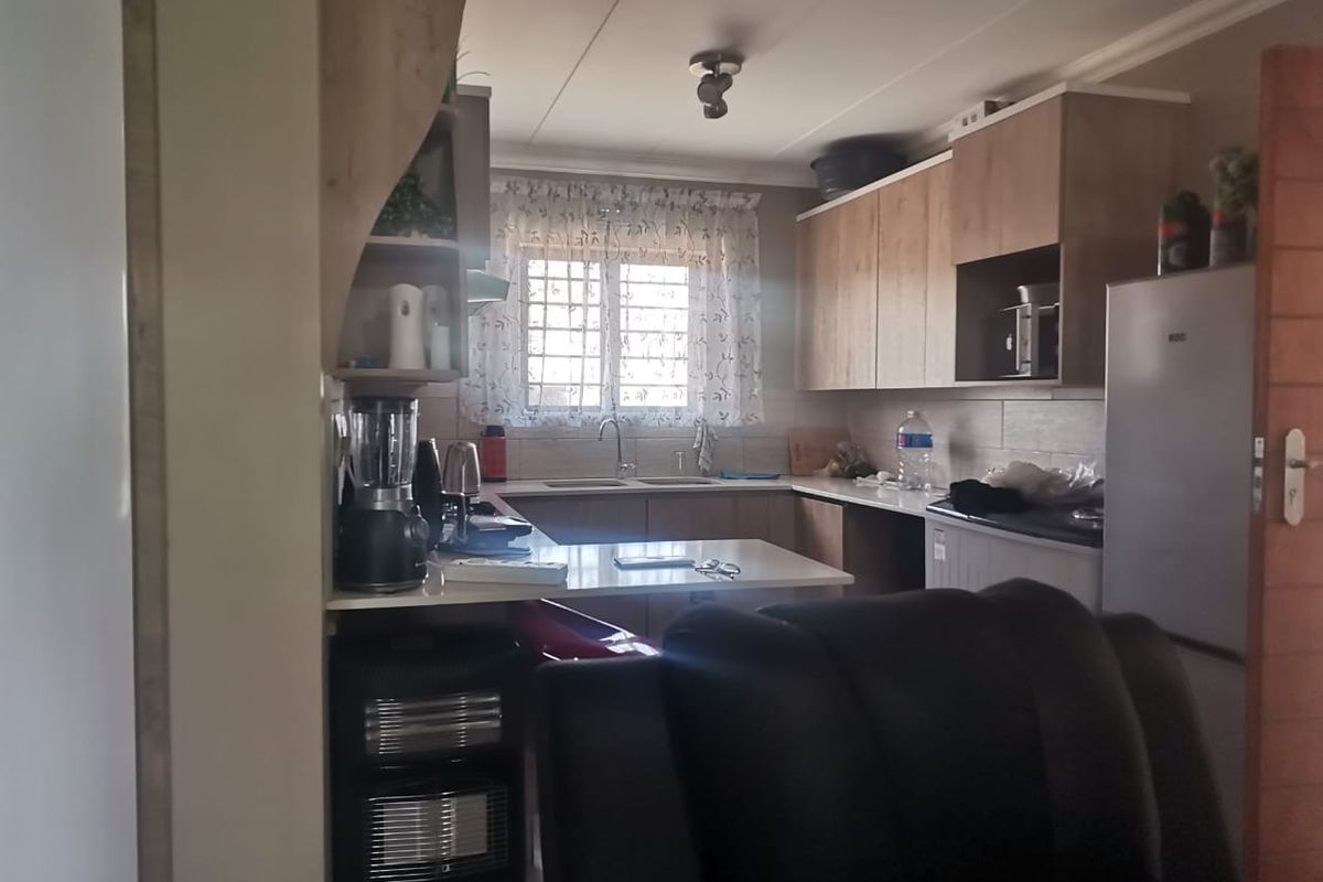 A functional kitchen featuring wood-look cabinetry, laminate countertops, a double sink, and tiled backsplash, offering a practical layout for daily meal preparation.
