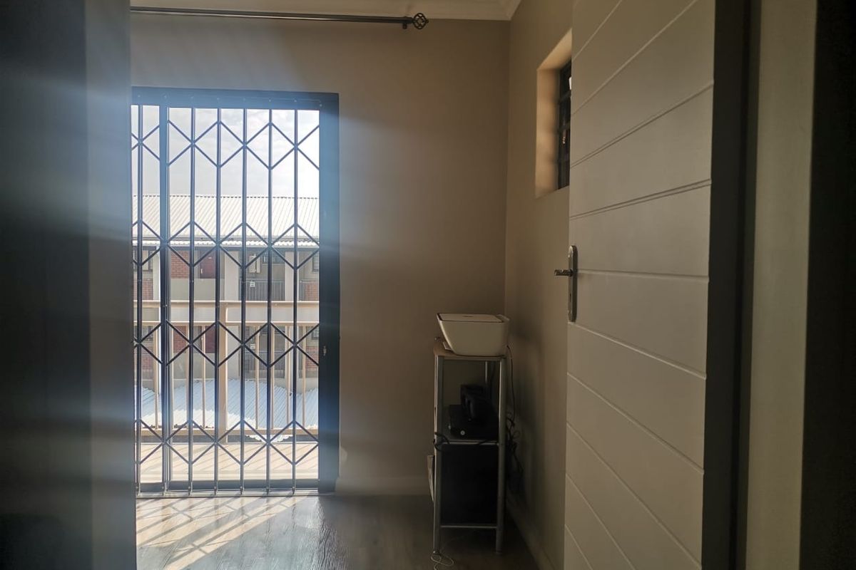 A bright, empty bedroom featuring laminate flooring, a sliding door with a security gate, and neutral wall tones.