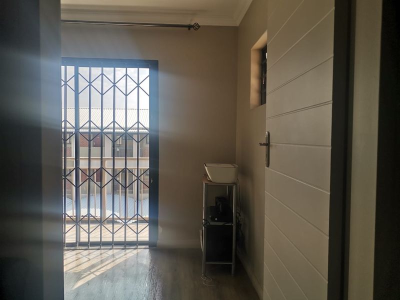 A bright, empty bedroom featuring laminate flooring, a sliding door with a security gate, and neutral wall tones.