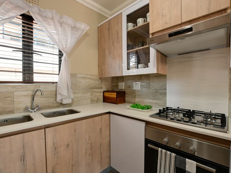 Modern kitchen featuring light wood-finish cabinetry, stone countertops, a stainless steel gas hob, built-in oven, and a double sink with tiled backsplash.