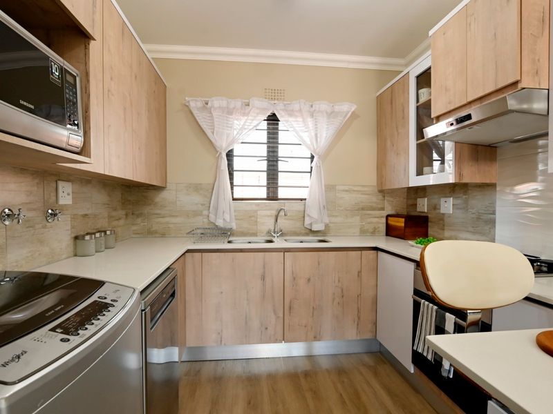 Modern kitchen featuring light wood-finish cabinetry, stone-look countertops, a double sink, integrated microwave, and extractor fan with a tiled backsplash.