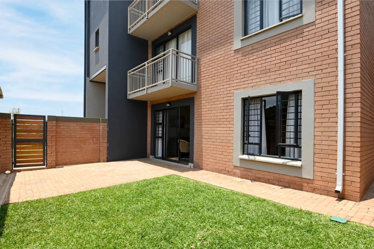 Rear view of the apartment building featuring a private paved patio, small lawn area, and balcony access from the living space.