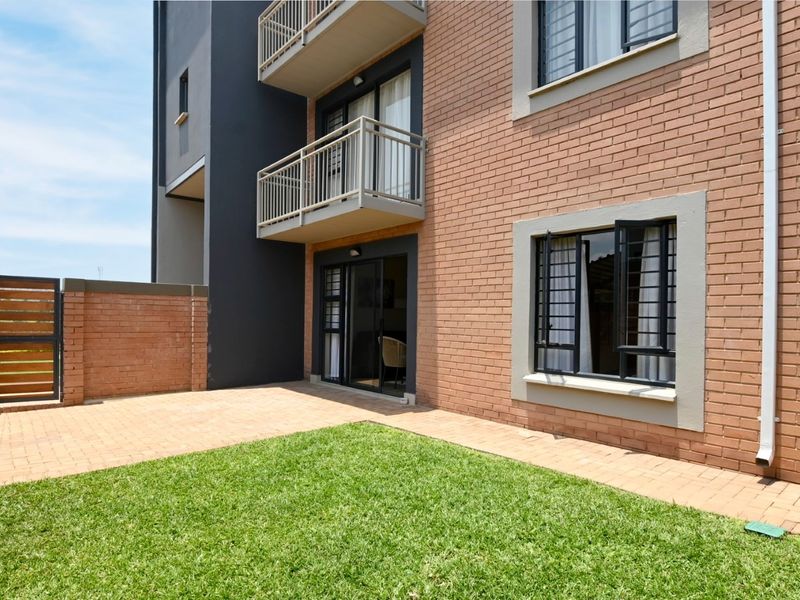 Rear view of the apartment building featuring a private paved patio, small lawn area, and balcony access from the living space.