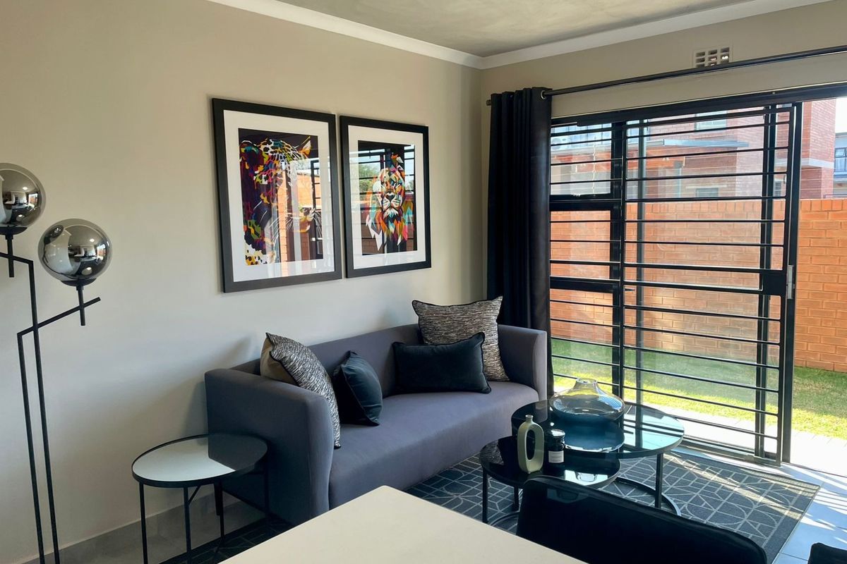 A well-maintained living room featuring tiled flooring, cove cornicing, and a large sliding glass door with integrated security gate leading to the exterior.
