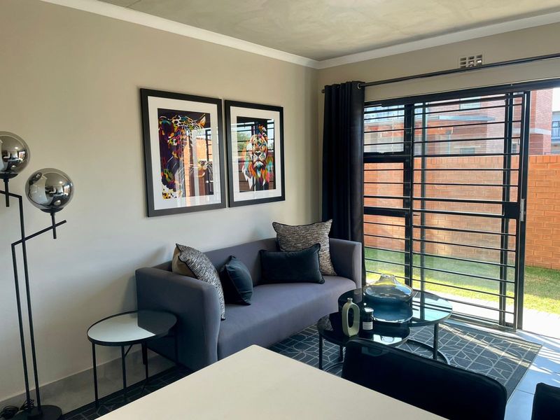 A well-maintained living room featuring tiled flooring, cove cornicing, and a large sliding glass door with integrated security gate leading to the exterior.