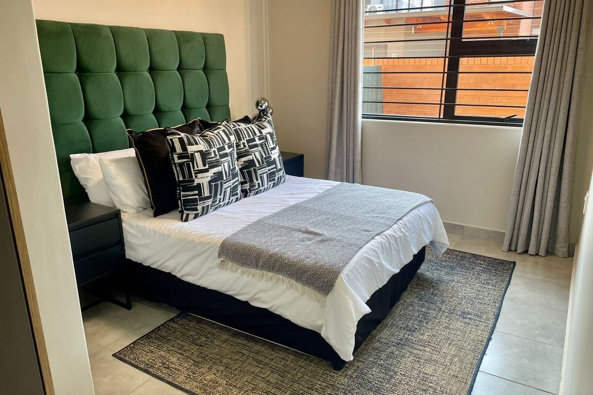A well-maintained bedroom featuring tiled flooring and a large window with security bars, providing natural light and a clean, modern aesthetic.