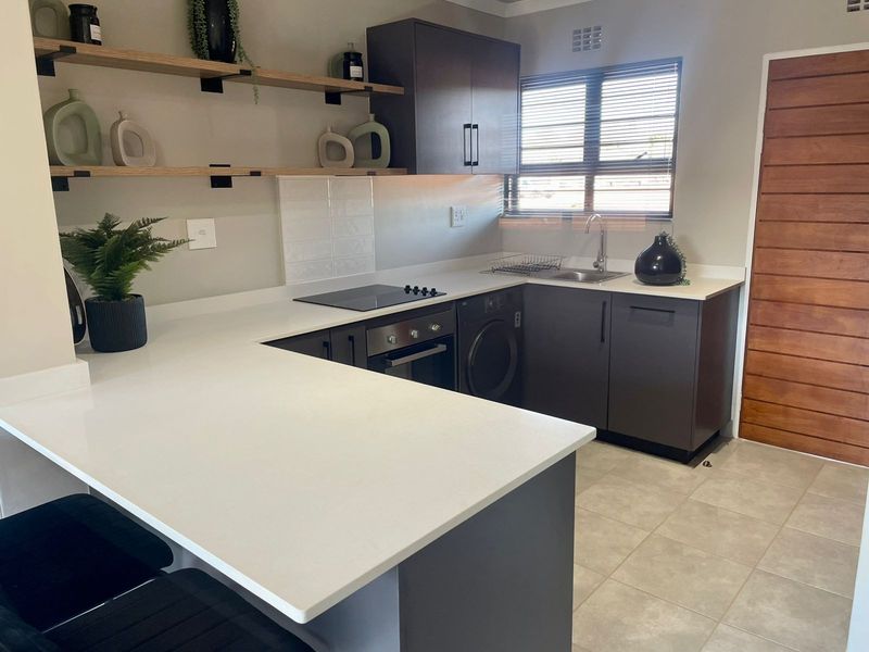 Modern kitchen featuring dark cabinetry, white quartz countertops, built-in oven, electric hob, and integrated laundry space with tiled flooring.