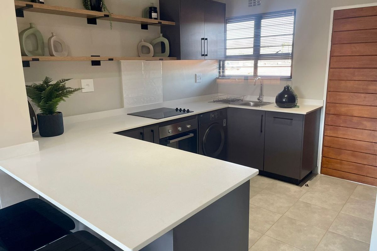 Modern kitchen featuring dark cabinetry, white quartz countertops, built-in oven, electric hob, and integrated laundry space with tiled flooring.