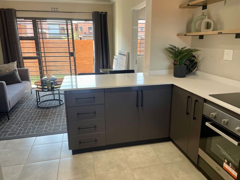 Modern open-plan kitchen featuring quartz countertops, built-in oven, and hob, seamlessly flowing into a living area with access to an outdoor patio.