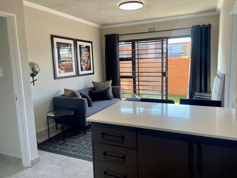 Modern open-plan living area featuring a kitchen island with stone countertop, tiled flooring, and a sliding glass door leading to the exterior.