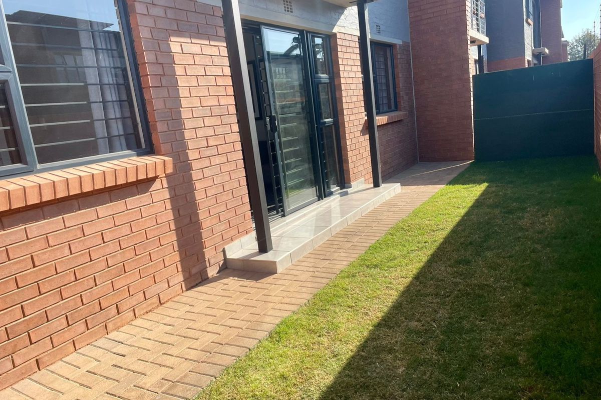 A private rear garden area featuring a paved walkway, brick exterior walls, and a sliding glass door providing access to the apartment interior.