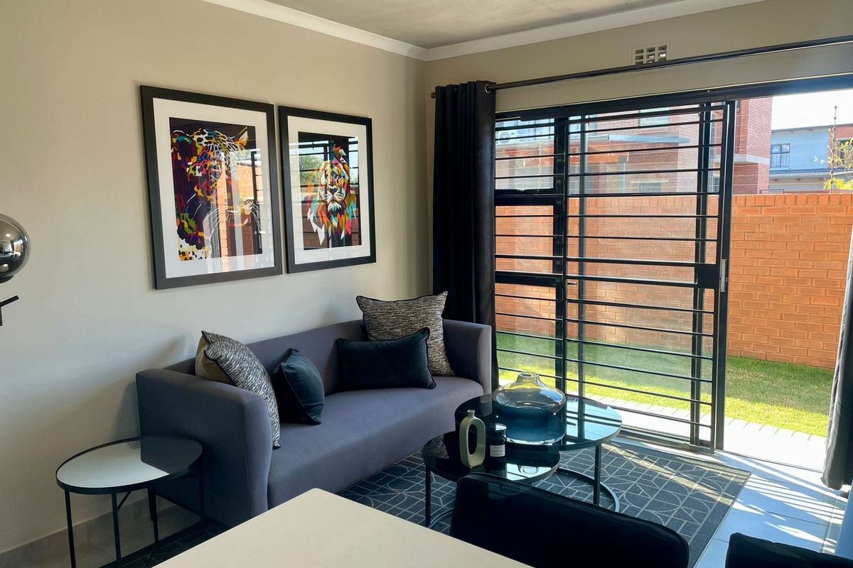 A well-maintained living room featuring tiled flooring, a sliding glass door with security gate, and access to an outdoor area.