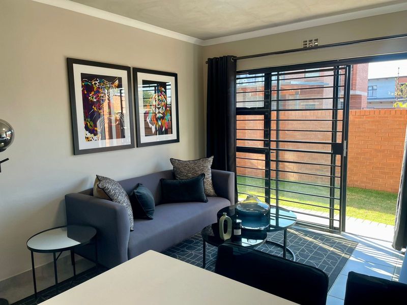 A well-maintained living room featuring tiled flooring, a sliding glass door with security gate, and access to an outdoor area.