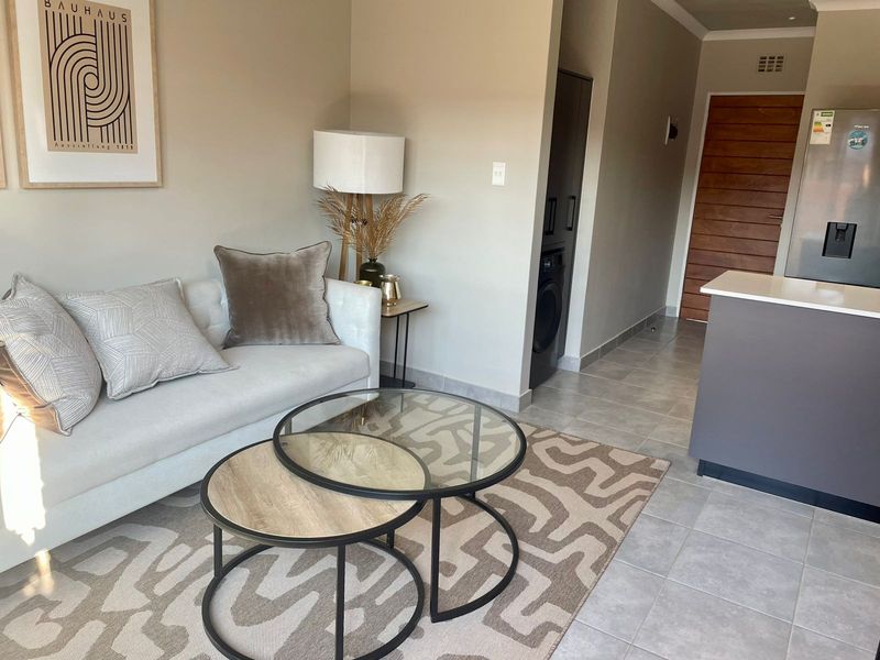 An open-plan living area featuring tiled flooring, a modern kitchen island, and a solid wood entrance door in a well-maintained apartment setting.