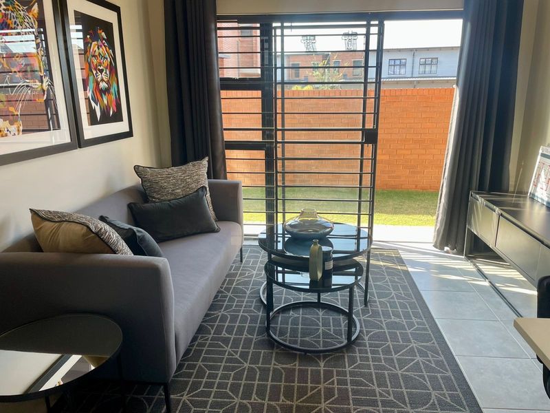 A well-lit living room featuring tiled flooring and a sliding glass door with a security gate, providing direct access to the outdoor area.