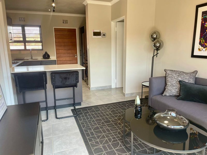 Open plan living area featuring a modern kitchen with breakfast bar, stone countertops, and neutral tiled flooring throughout the space.