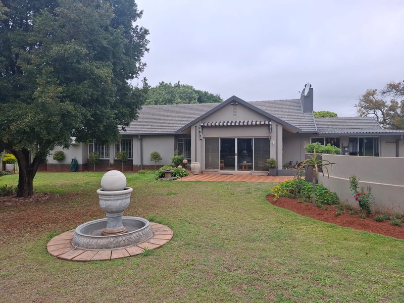 Rear view of the house featuring a tiled roof, sliding glass doors leading to a brick patio, and a well-maintained garden with a water feature.