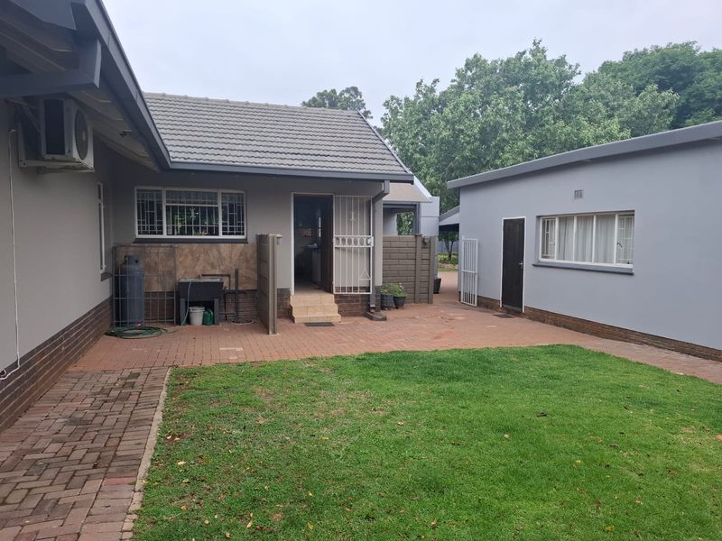 A well-maintained rear exterior view featuring a paved patio area, a small lawn, and access to the main house and a separate outbuilding.