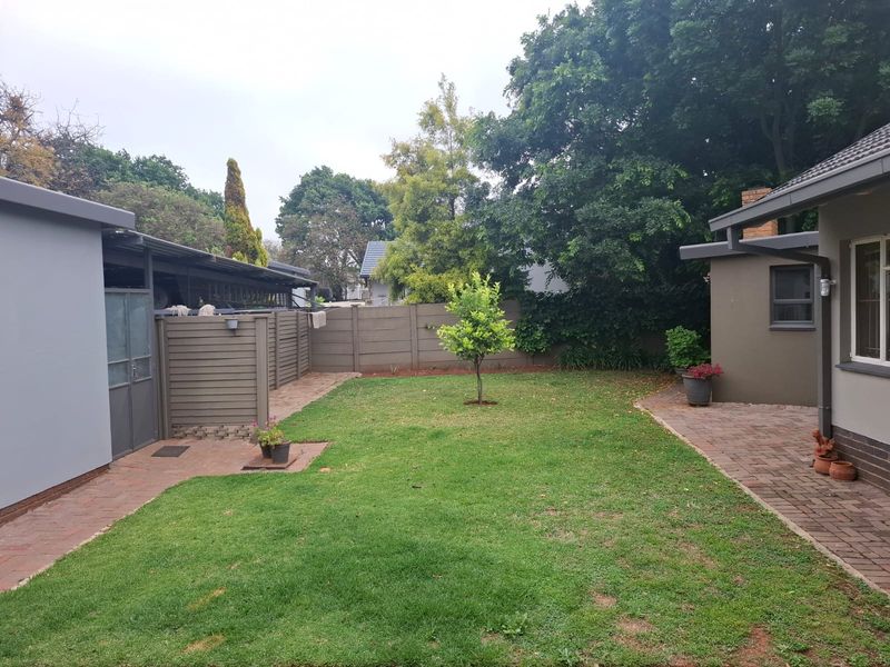 A well-maintained rear garden featuring a central lawn, brick paved pathways, and perimeter boundary walling, providing a private outdoor space.