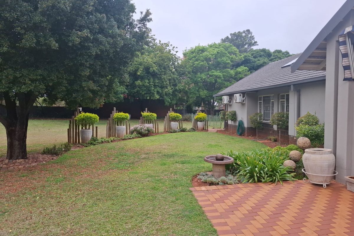 A well-maintained rear garden featuring a paved patio area, established lawn, and mature trees, providing a private outdoor space.