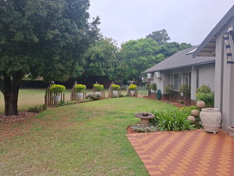 A well-maintained rear garden featuring a paved patio area, established lawn, and mature trees, providing a private outdoor space.