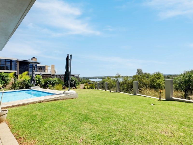 Outdoor pool area featuring a paved patio, well-maintained lawn, and perimeter fencing with scenic views.
