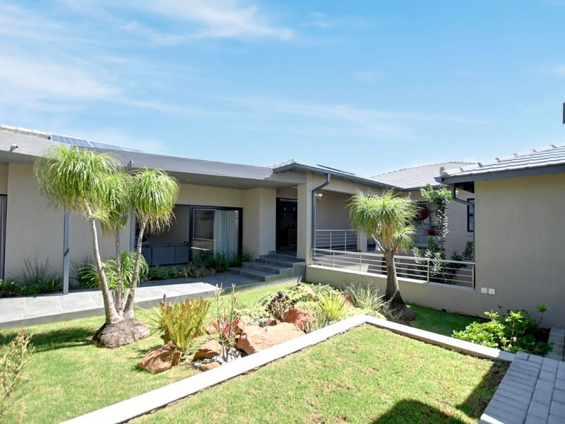 A well-maintained rear exterior view featuring a landscaped garden, paved walkways, and a covered patio area with modern architectural finishes.