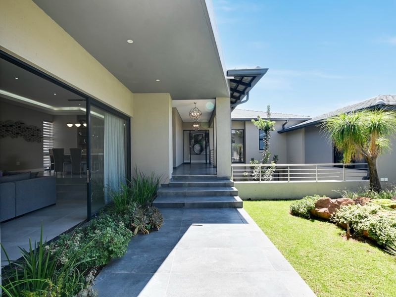 A modern covered patio featuring large sliding glass doors, tiled flooring, and steps leading to a landscaped garden area.