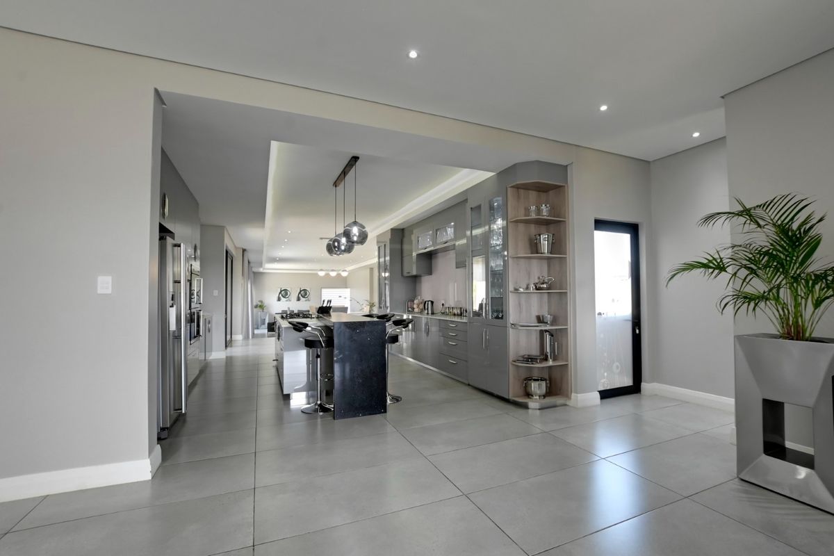 Modern, high-end kitchen featuring sleek grey cabinetry, a central island with stone countertops, recessed lighting, and large format floor tiles.